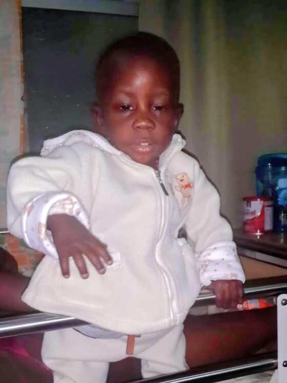 A young child stands in a hospital cot during treatment.